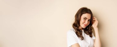 Close up portrait of coquettish beautiful girl gazing silly, gently smiling and giggling, posing flirty and cute against beige background. Women beauty and valentines concept.