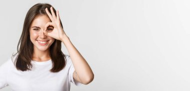 Çekici, kendine güvenen, mutlu gülümseyen ve göze güzel bir jest yapan kızın yakın çekimi..