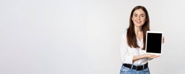 Portrait of corporate woman showing tablet screen, demonstrating company website, standing over white background.