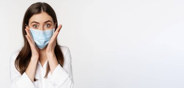Covid-19 ve pandemik konsept. Coronavirus sosyal mesafesi sırasında tıbbi maske takan genç bir ofis kadını beyaz arka planda duruyor..