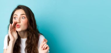 Şirin dedikoducu kız dedikodu yayıyor, birine haber veriyor, mavi arka planda dikiliyor..