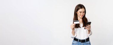 Akıllı telefon ekranına bakan genç bir kadının portresi, internetten kredi kartıyla ödeme yapmak, beyaz arka planda durmak, sipariş vermek..