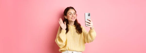友好女孩在视频聊天应用程序上说话 在智能手机摄像机前挥手 在手机上交谈 站在粉色背景下的肖像 — 图库照片