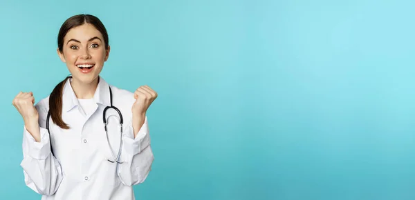 幸せと興奮若い女性医師 医師のお祝い 目標を達成し 青の背景に白いコートに立って — ストック写真