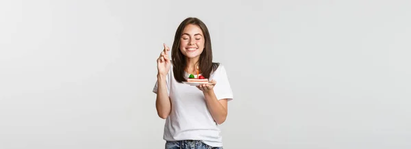 축하하는 미소짓는 소녀는 손가락을 교차하며 케이크를 불면서 소원을 — 스톡 사진