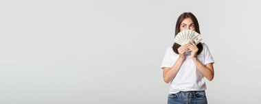 Heyecanlı hayalperest kız elinde para tutuyor ve sol üst köşeye bakıyor, beyaz arka planı düşünüyor..
