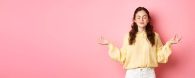 O rahatladı. Gülümseyen barışçıl genç kız meditasyon yapıyor, zen jestinde el ele tutuşuyor, gözlerini kapatıyor, rahatlamış ve sakin hissediyor, pembe arka planda duruyor..