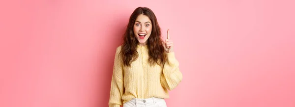 穿着时髦服装的年轻而兴奋的女人 竖起手指 提建议 提建议 提出有趣的计划 站在粉色的背景上 — 图库照片
