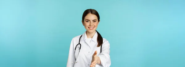 笑顔のプロの女性医師 手を伸ばしセラピスト 握手ジェスチャー 医療クリニックや病院で患者を迎える 青の背景の上に立って — ストック写真