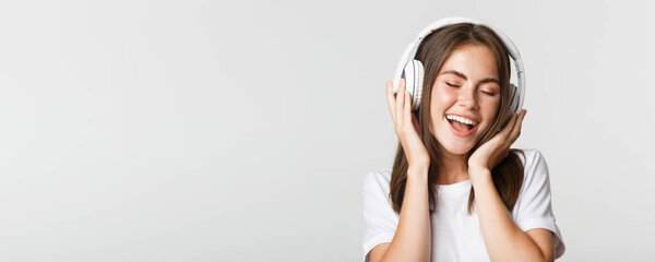 Крупный план привлекательной счастливой женщины слушающей музыку в беспроводных наушниках, поющей вместе.