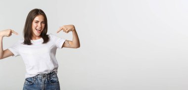 Kendine güvenen çekici esmer kız gülümsüyor, kendini işaret ediyor..