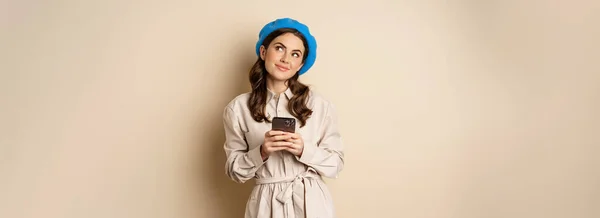 Dreamy Smiling Woman Stylish Trenchcoat Looking Fantasizing While Shopping Mobile — Stockfoto