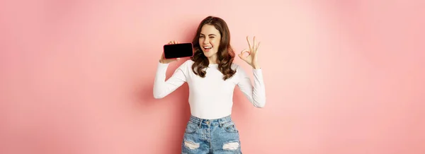 Счастливая Подмигивающая Девушка Демонстрирующая Фирменный Магазин Мобильное Приложение Показывающая Смартфон — стоковое фото