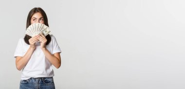 Heyecanlı hayalperest kız elinde para tutuyor ve sol üst köşeye bakıyor, beyaz arka planı düşünüyor..