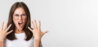 Gözlüklü kızgın ve öfkeli genç bir kadının beyaz arka plan hakkında yakınması..