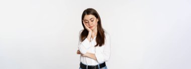 Unamused, bored brunette woman looking gloomy and sad, sighing, standing reluctant over white background.