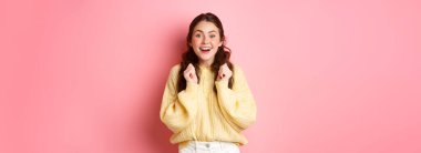 Kameraya bakan, kazanmak isteyen, önemli sonuçları bekleyen, pembe arka plana karşı duran, umut dolu şanslı bir kızın görüntüsü..