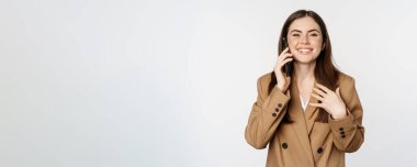 Businesswoman having mobile call, conversation on smartphone, talking with client, standing over white background in brown suit.