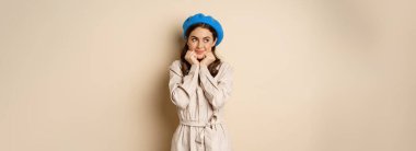 Portrait of beautiful woman in trendy outfit, touching her face and looking dreamy, yearning smth, standing against beige background. People concept