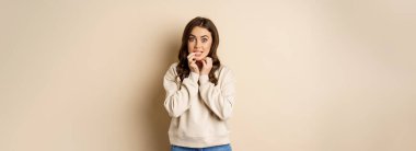 Portrait of woman looking with interest and yearning, biting finger, wants to try taste smth, standing over white background.
