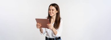 Portrait of beautiful girl smiling, looking happy, watching on digital tablet, standing against white background. Copy space