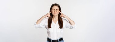 Annoyed girl shut ears from loud sound, discomfort of hearing smth noisy, standing bothered against white background.