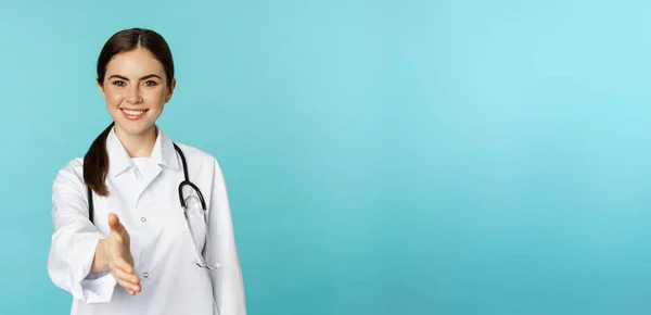 微笑专业女医生 治疗师伸出手 在诊所或医院问候病人 站在蓝色背景之上 — 图库照片