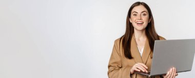 Portrait of corporate woman working with laptop, smiling and looking assertive, white background.