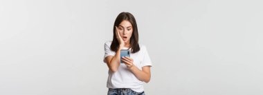 Şok olmuş ve etkilenmiş esmer kız akıllı telefon ekranına hayret ediyor..