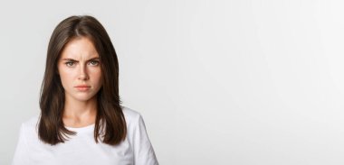 Close-up of pissed-off young girl frowning and looking angry at camera, white background.