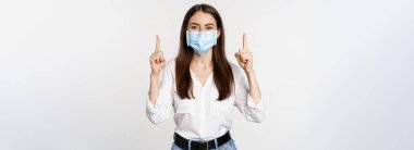 Coronavirus 'tan gelen tıbbi maskeli kurumsal bir kadının portresi, işaret eden, reklam veren, beyaz arka plan.