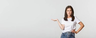 Şüpheci ve eğlendirilmemiş genç rahatsız kız omuz silkiyor, bir elini kaldır..