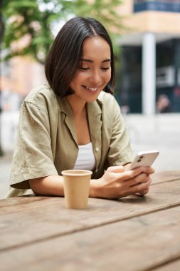 Genç bir kadının kahvesini yudumlarken portresi, şehirdeki bankta içki içerken, akıllı telefon kullanırken. Boşluğu kopyala