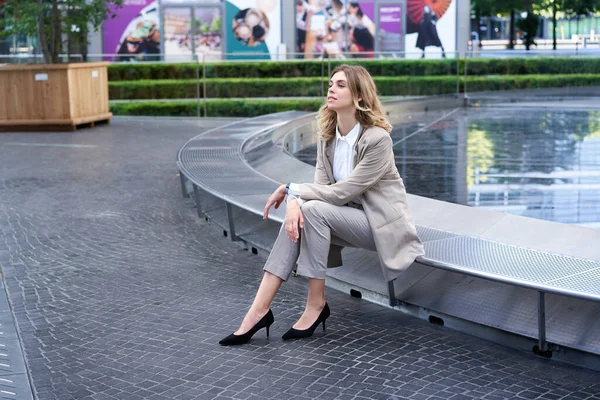 stock image Beautiful female corporate woman in suit, sitting alone near fountain in business centre.