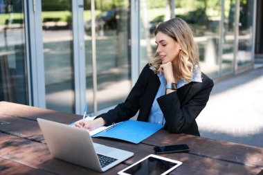 Açık havada çalışan başarılı bir iş kadını. Şirket kadını dizüstü bilgisayarla bankta oturuyor, yazıyor, iş toplantısı sırasında notlar alıyor..