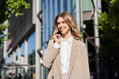 İş kadını portresi telefon görüşmesi yapıyor, ofis binasının yanındaki caddede duruyor, telefonda biriyle konuşuyor..