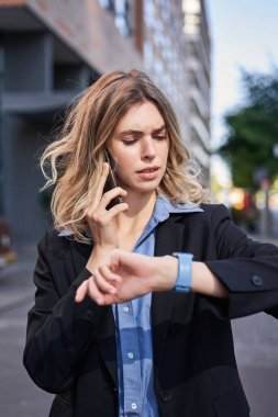 İş kadınının dikey portresi telefon görüşmesi yapıyor, dijital saatine bakıyor, cihazdaki mesajları okuyor..