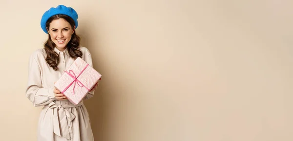 stock image Holidays and gifts concept. Beautiful girl receive gift box and looking happy, holding pink wrapped present with joyful face expression, beige background.