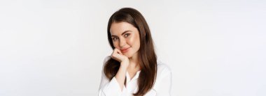 Close up of beautiful, coquettish brunette woman, blushing and smiling flirty, posing against white background. Copy space