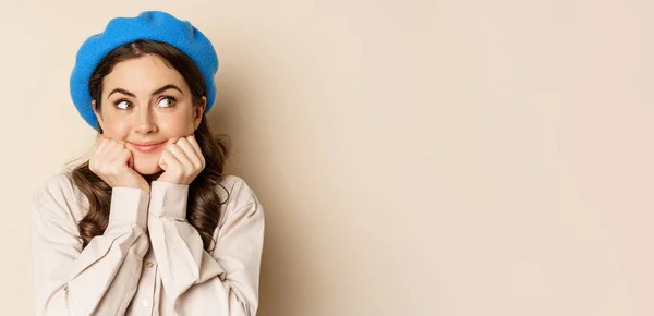 stock image Cute coquettish woman posing, smiling and looking aside with thinking, dreamy face, imaging smth, standing over beige background.