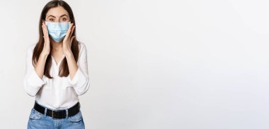 Şaşırmış yüz maskeli kadın hayrete düşmüş görünüyor, harika haberlere bakıyor, büyük açığa vuruyor, beyaz arka planda duruyor..