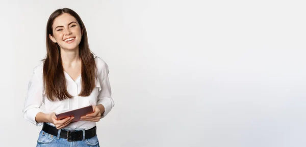 stock image Smiling modern woman standing with digital tablet, laughing and looking happy, working, posing against white studio background.