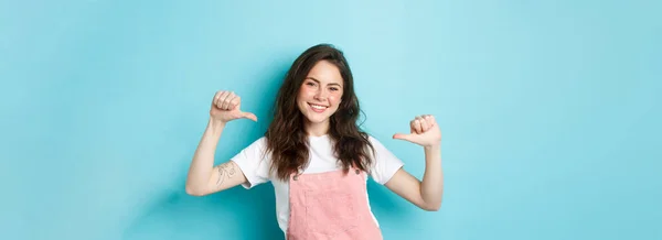 stock image Young smiling woman pointing at herself, looking confident and happy, self-promoting, talking about her, personal achievement, standing over blue background.