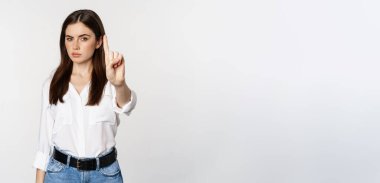 Serious woman showing taboo, stop gesture, shaking finger in disapproval, disagree, forbidding something, standing over white background.