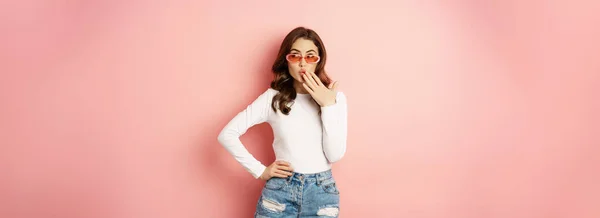 stock image Coquettish and stylish brunette girl, laughing and smiling, wearing sunglasses, wearing white blouse and jeans, pink background. Copy space