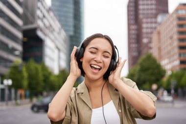 Şehirde kendini mutlu hisseden dansçı kız. Asyalı kadın dans ediyor ve kulaklıkla müzik dinliyor, sokakta poz veriyor..