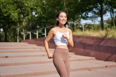 Refah ve spor. Asyalı fitness koşucusu, parkta koşan, tozluklarla sokakta koşan, mutlu bir şekilde gülümseyen..