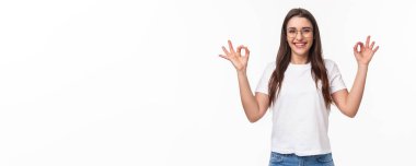 Gözlüklü ve tişörtlü mutlu, çekici bir kızın belden yukarı portresi, onaylama işaretlerini gösteriyor, olumlu yanıt verin, iyi ürün önerin veya değerlendirin, anlaşma değil, beyaz arka plan.