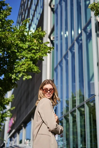 Stock image Portrait of confident office lady, business woman in sunglasses posing outdoors, near her company office building, wearing beige suit.