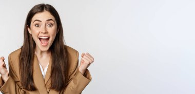 Enthusiastic girl screaming and rejoicing, looking at camera, winning, celebrating victory and triumphing, standing over white background.